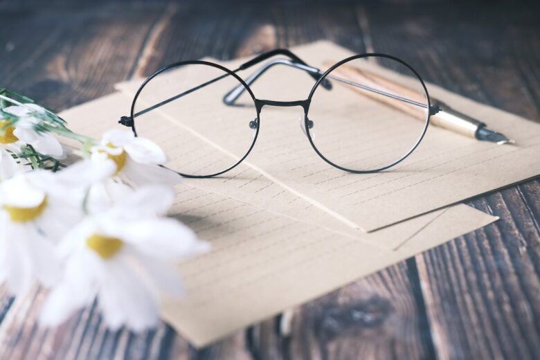 Glasses, flowers, a pen, and two papers on the wooden table