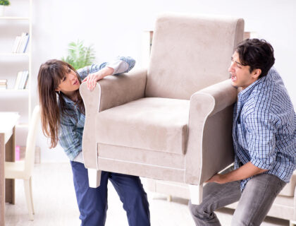 A couple struggling with moving the armchair in the living room