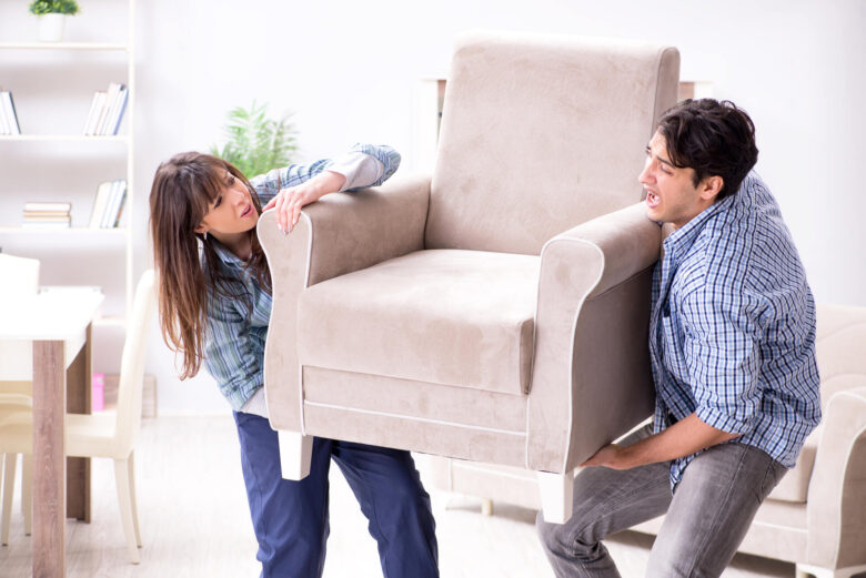 A couple struggling with moving the armchair in the living room