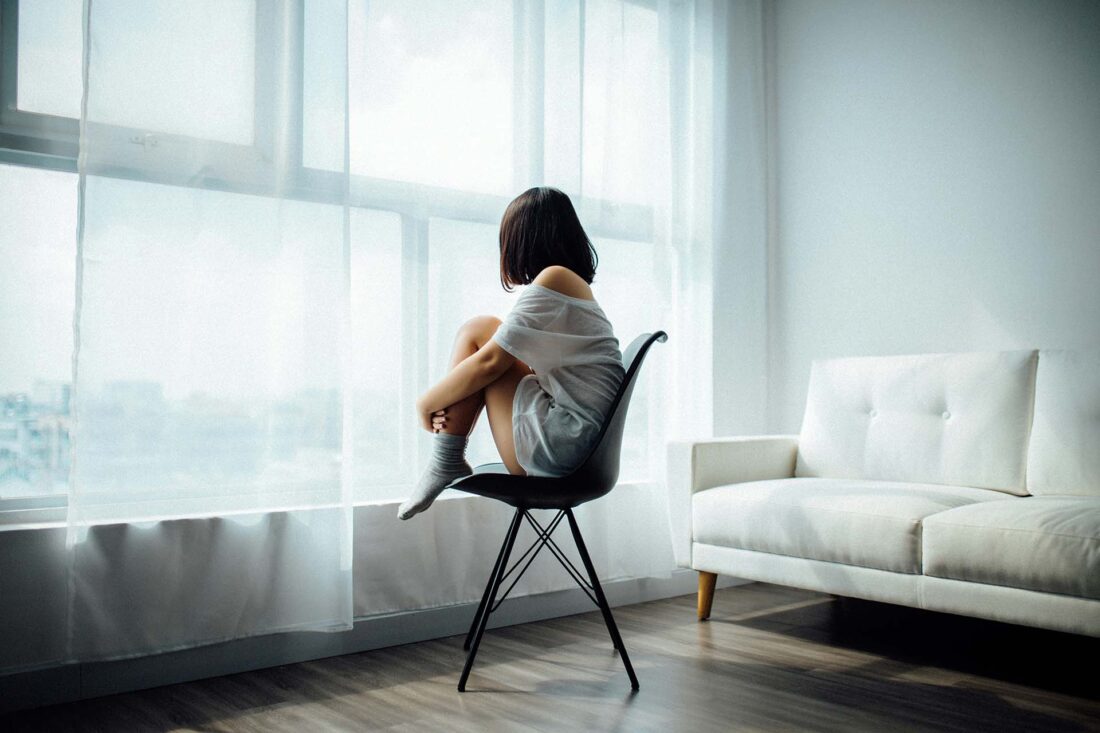 A sad woman sitting on a chair and looking out the window