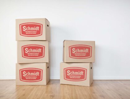 Stacked moving boxes on a laminated wooden floor in an empty room with a white wall.