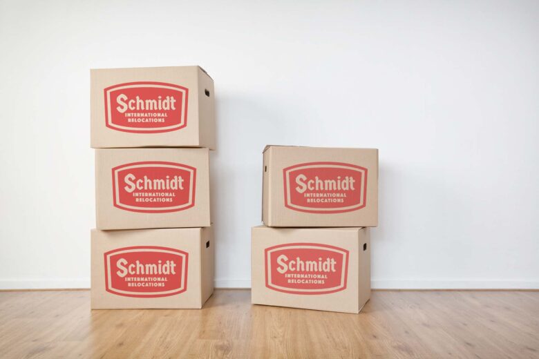 Stacked moving boxes on a laminated wooden floor in an empty room with a white wall.