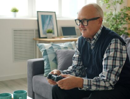 Elderly man playing video games on a couch. Active and fun retirement lifestyle.