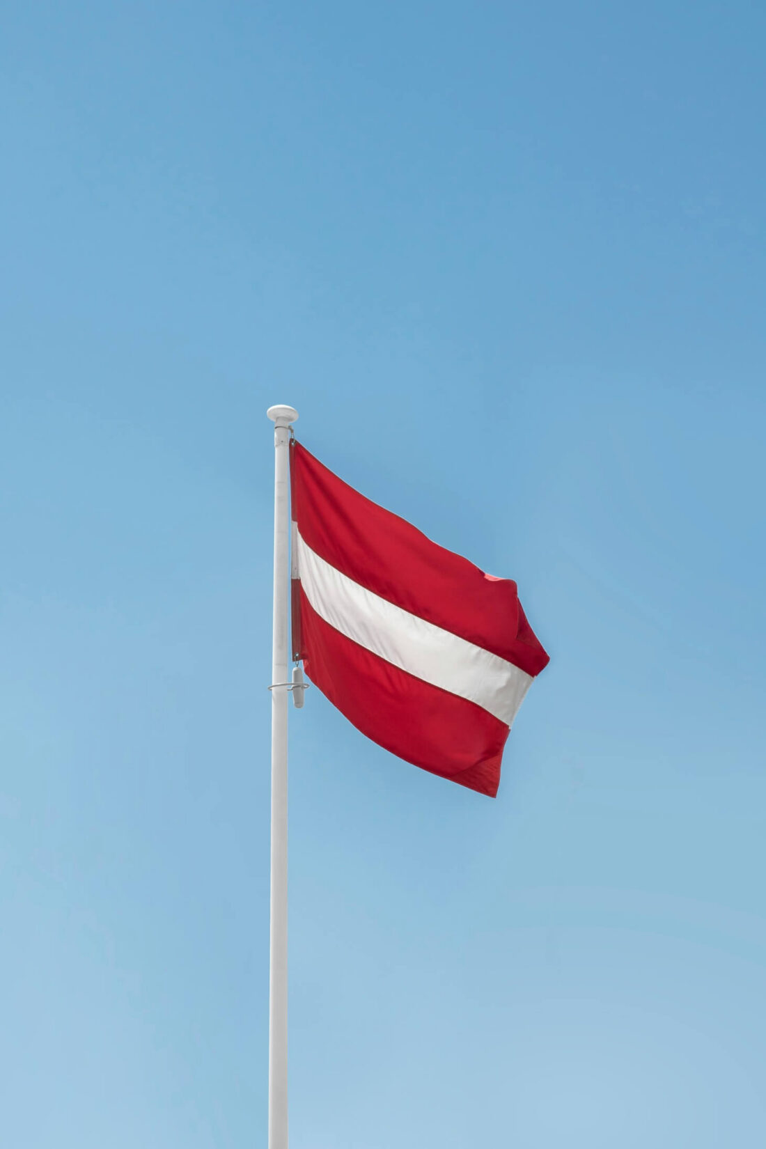 A red and white flag fluttering on a flagpole against a clear sky.