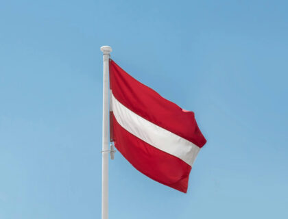 A red and white flag fluttering on a flagpole against a clear sky.