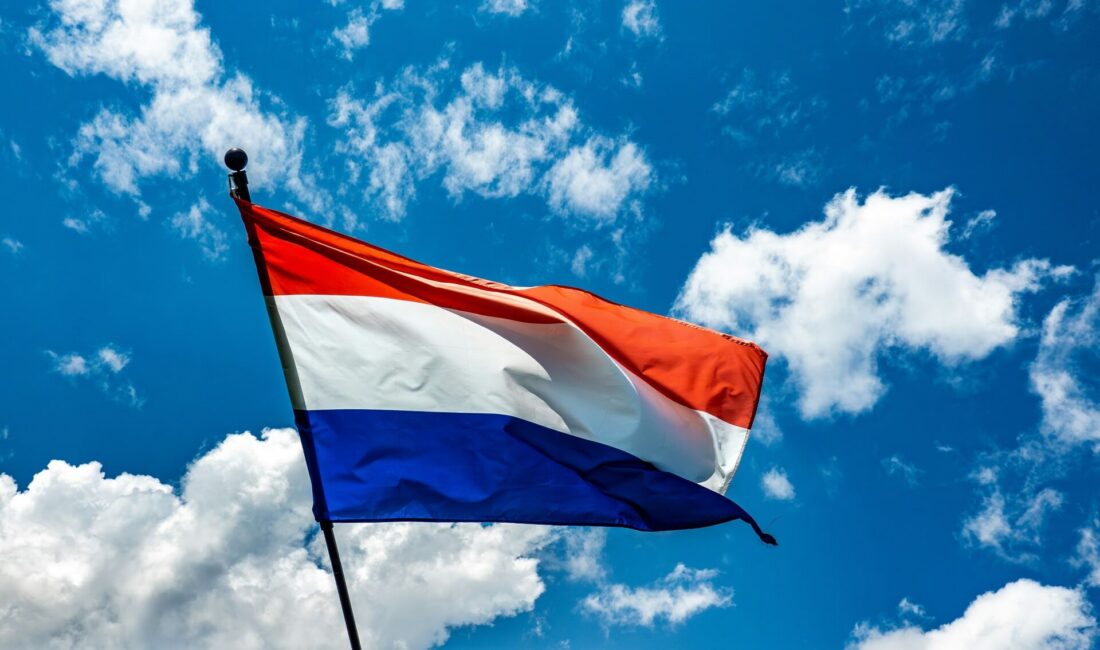 Red, white, and blue flag flying in the sky against a bright blue background.