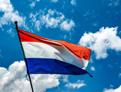 Red, white, and blue flag flying in the sky against a bright blue background.